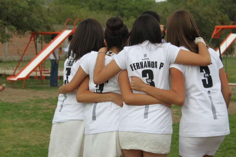 three girls in white shirts and shorts in front of a playground