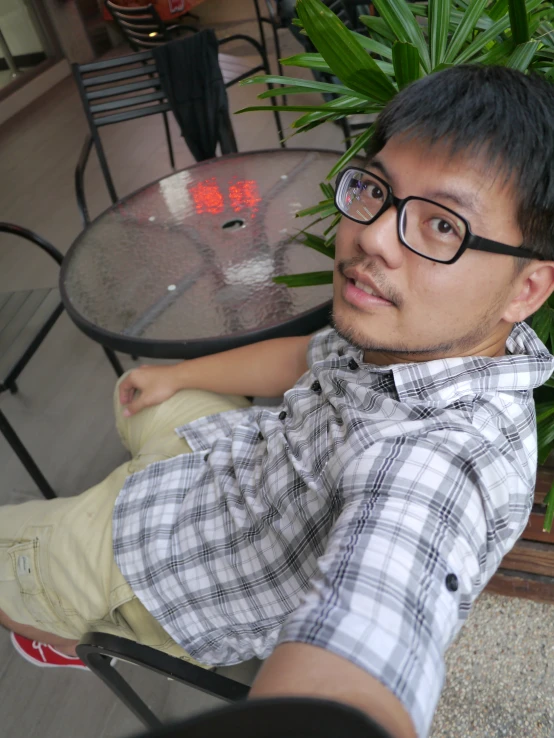 an asian man wearing glasses sitting in a chair with his arm around the shoulder