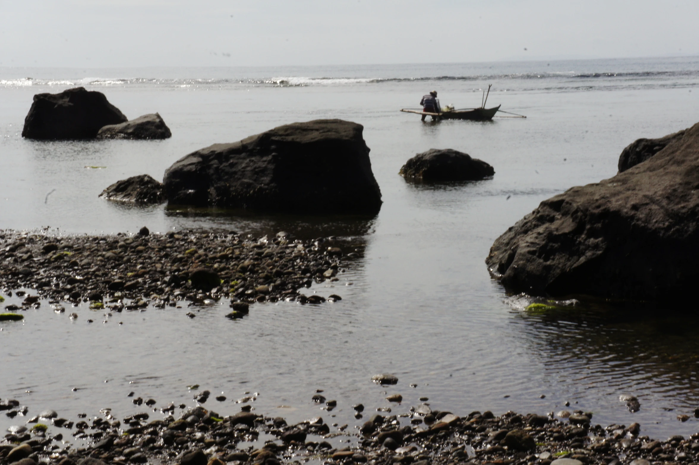 two people in small boats floating on water near large rocks