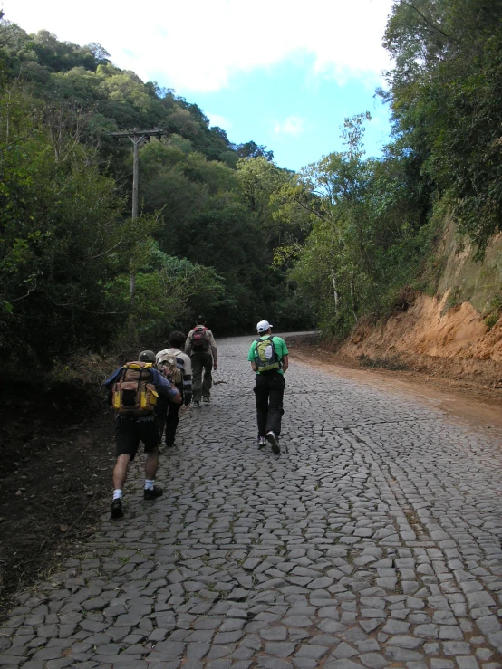 a group of men wearing backpacks walk up a road