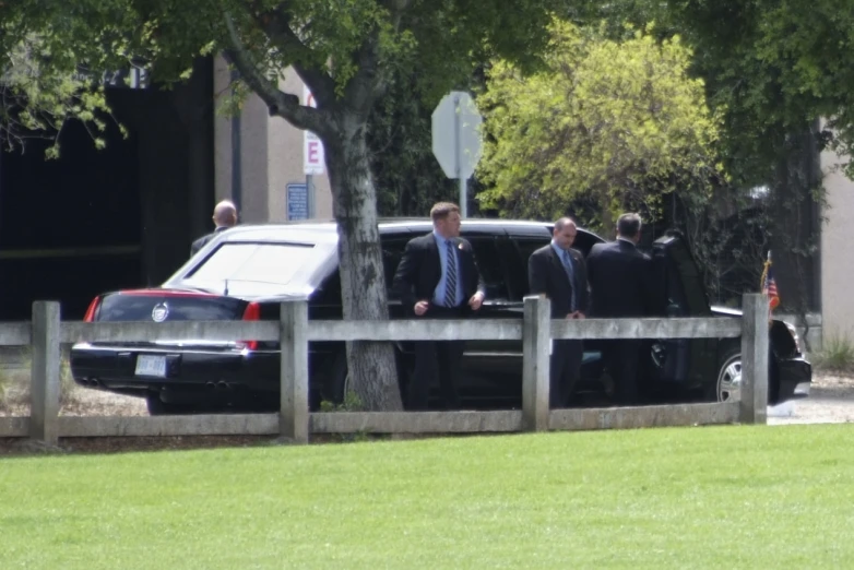 four men in suits standing behind a limousine