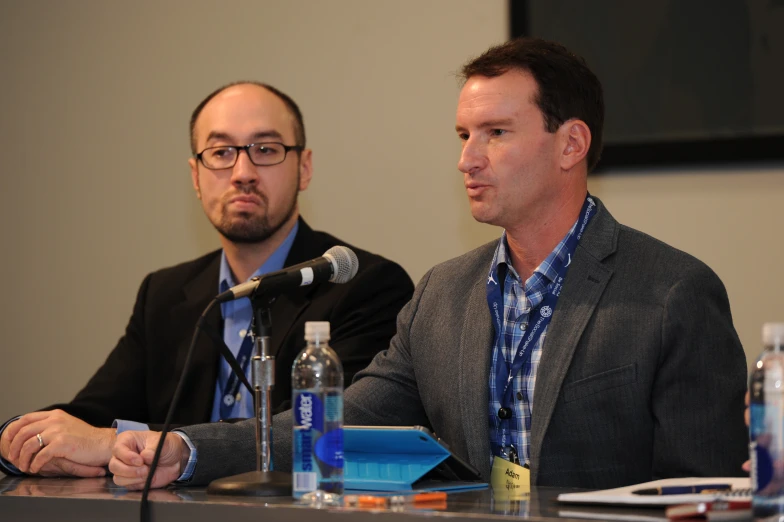 two men at a conference, one with glasses on and the other without glasses on