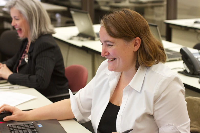 two woman work on laptops at a long desk