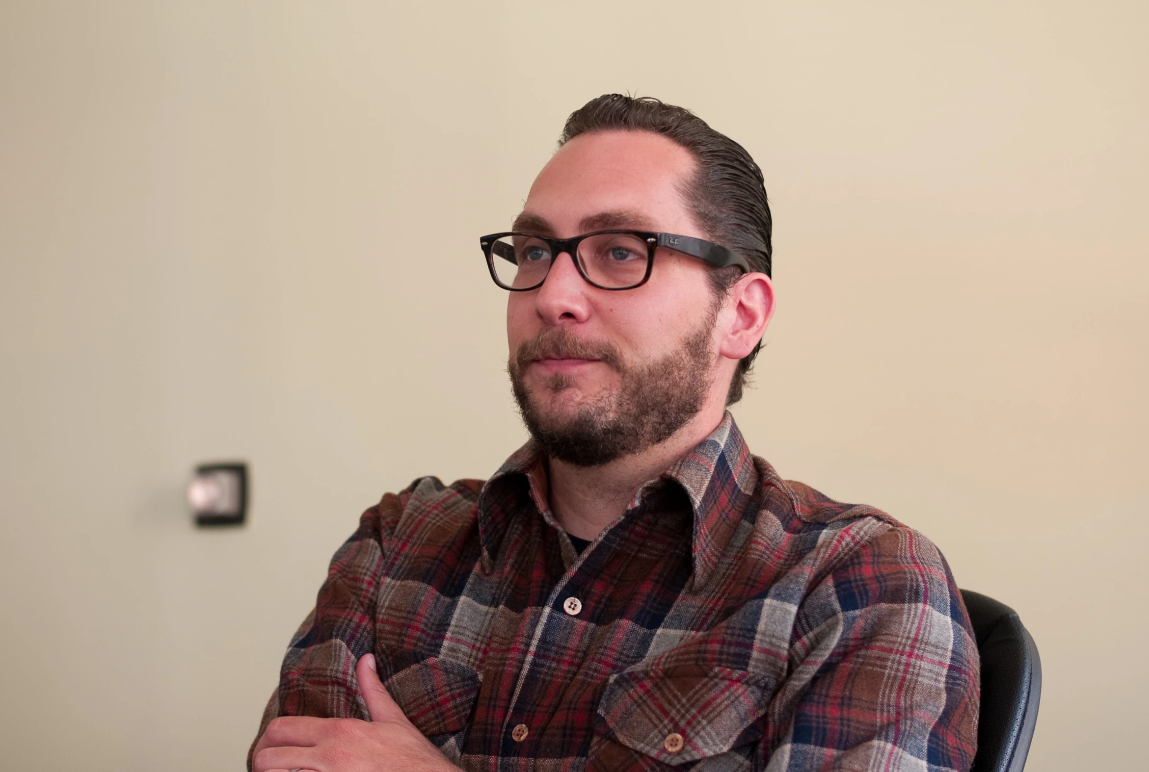 a man with glasses is wearing a plaid shirt and looking away from the camera