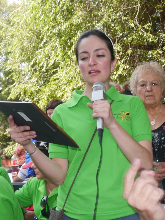 a young woman in a green shirt holding a tablet with two hands