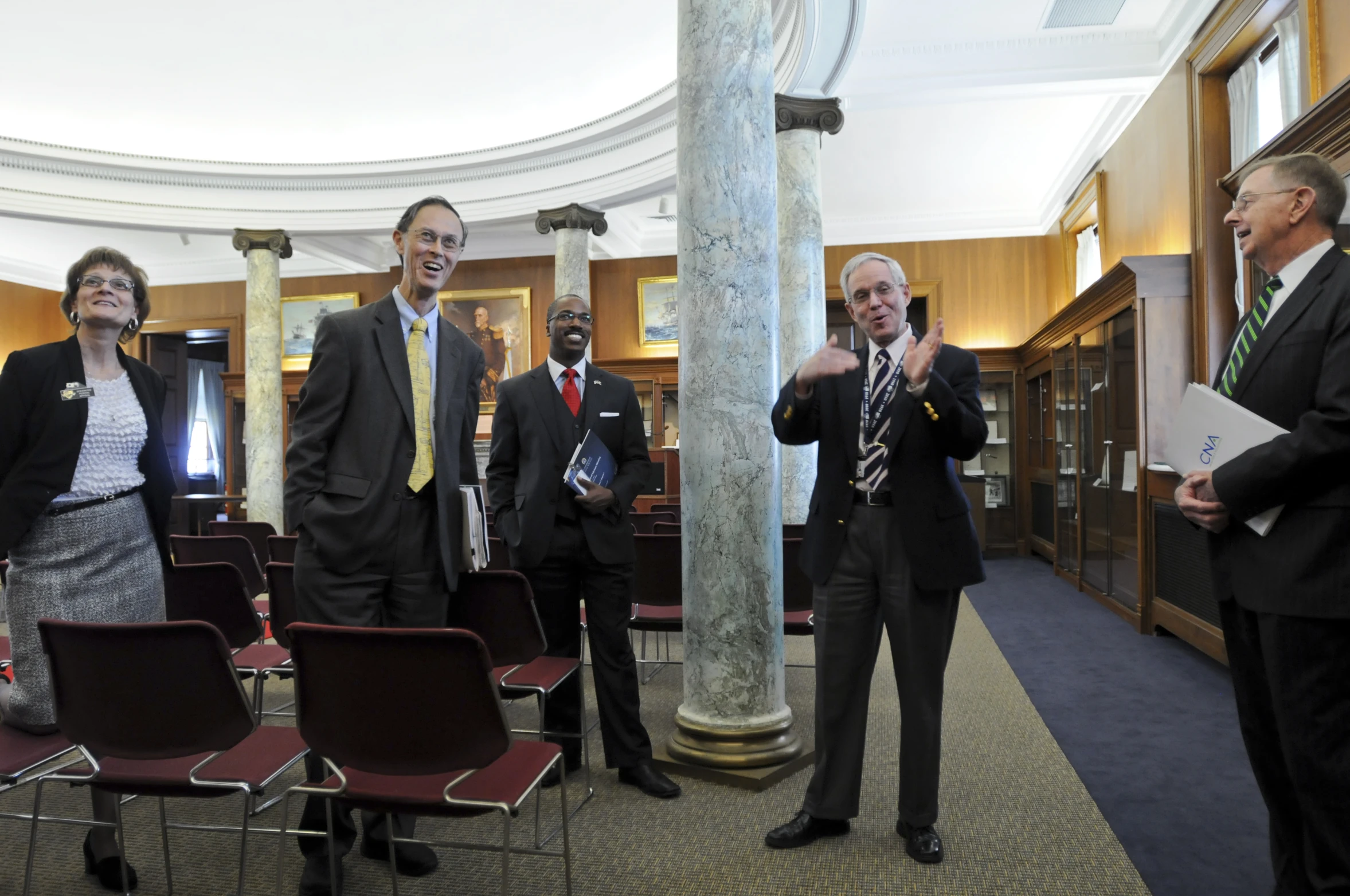 several men and women with ties are standing in a room with columns