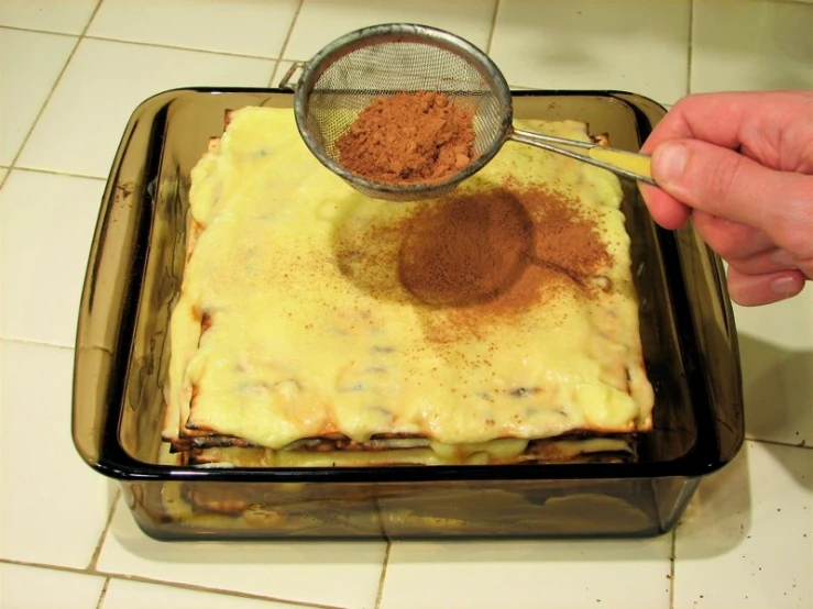 a person with a strainer scooping spices into the cake