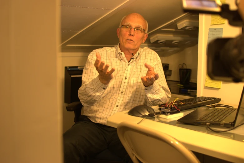 an older man sits at his desk with a camera attached to the side