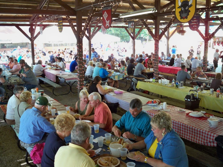 people eating at a wooden picnic shelter with tables covered with red checkered table cloths