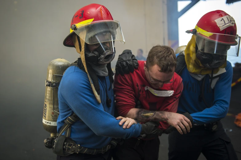 three firefighters are tackling soing on a mans arm