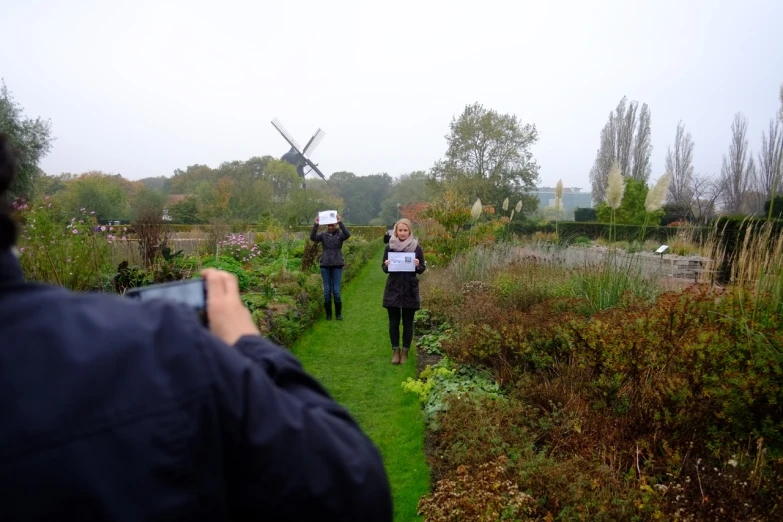 three people are walking in the grass in front of a windmill