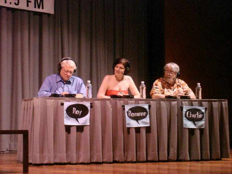 four people sit behind a table on stage and sign up a contest