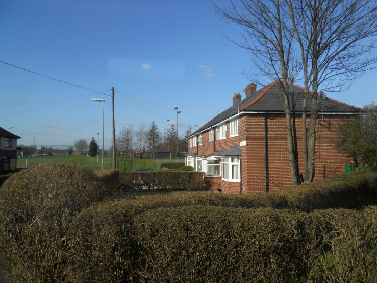 a red brick house is viewed through the bushes