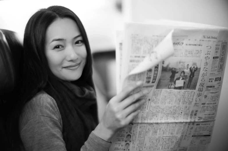 a woman reading a newspaper and smiling for the camera