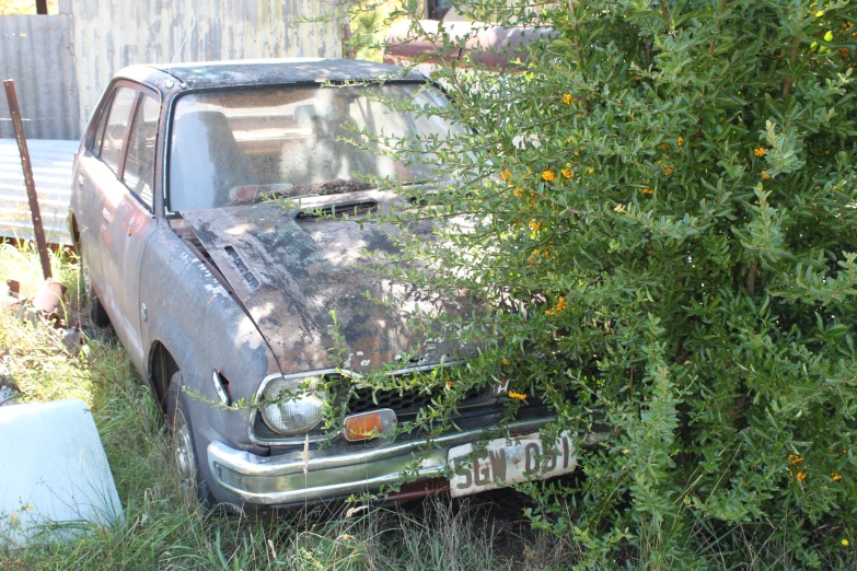 an old car is parked in the weeds outside