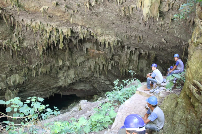 people sitting on the edge of a cliff and observing a cave