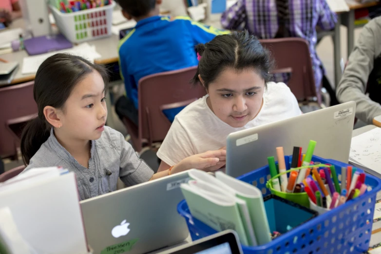 two children sit at the table, working on their computers