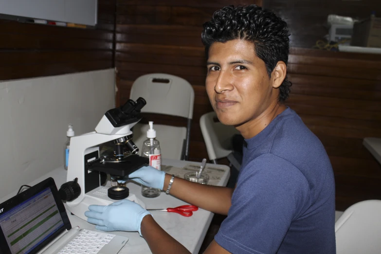 a man sitting in front of a microscope looking at the camera