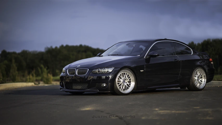 a black car sitting next to a forest on a street