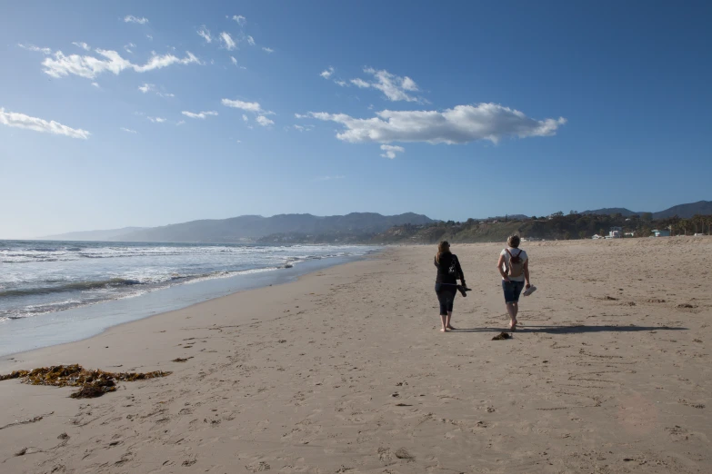 a couple of people walking on top of a sandy beach