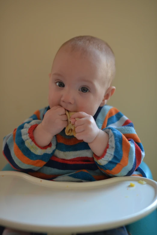 a baby boy is eating in a highchair