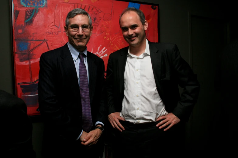 two men pose for the camera in front of a large red painting