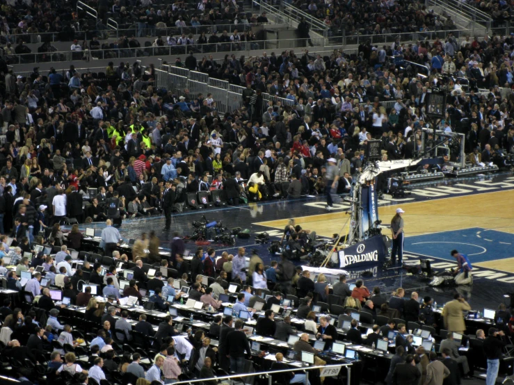 an audience stands at the center of a basketball court with a speaker