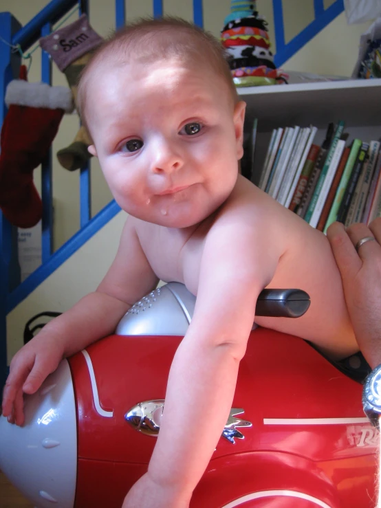 a toddler smiles for a picture atop a red plastic firetruck