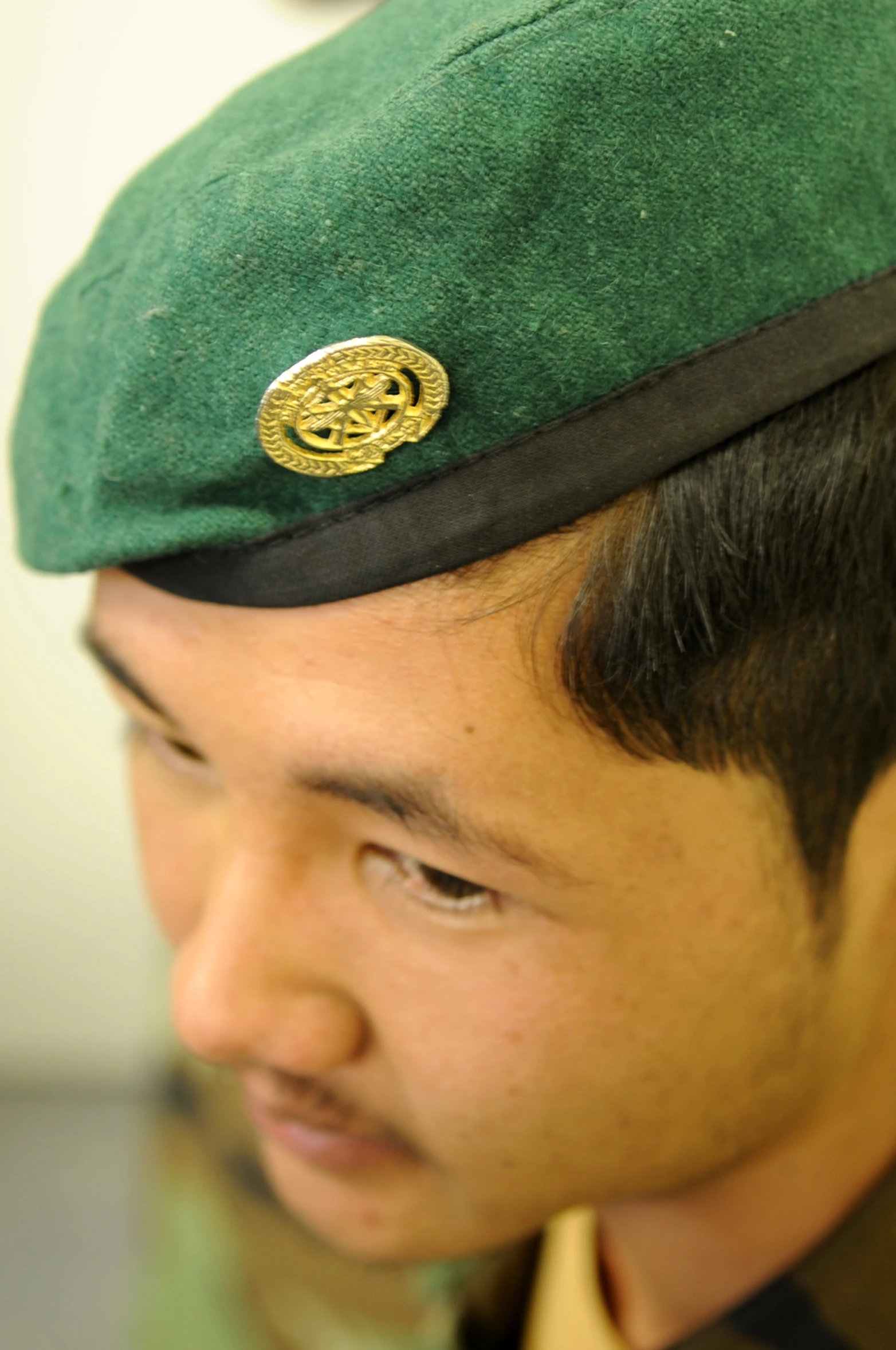 a man with a green hat is wearing a gold embroidered pin on his forehead