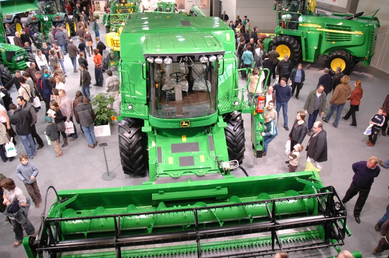 people in a large room watching a row of green tractors