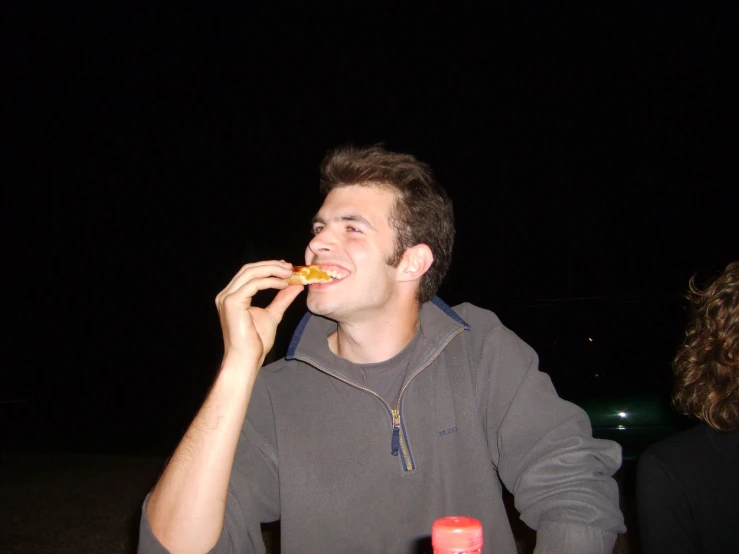 a man eating pizza next to a woman in the dark