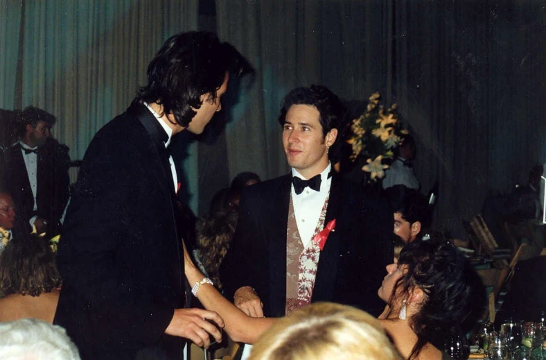 two men in formal clothing standing near each other at a banquet