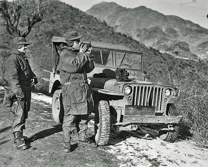 two men standing near an old military jeep