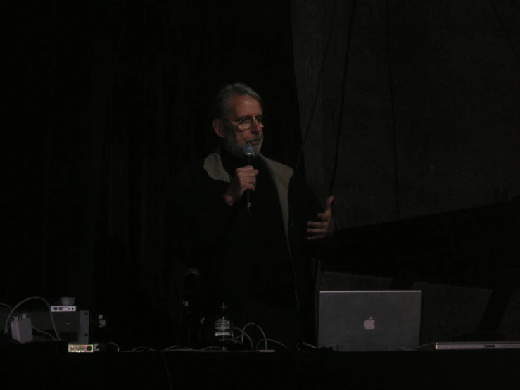 a man stands in front of a microphone and a laptop