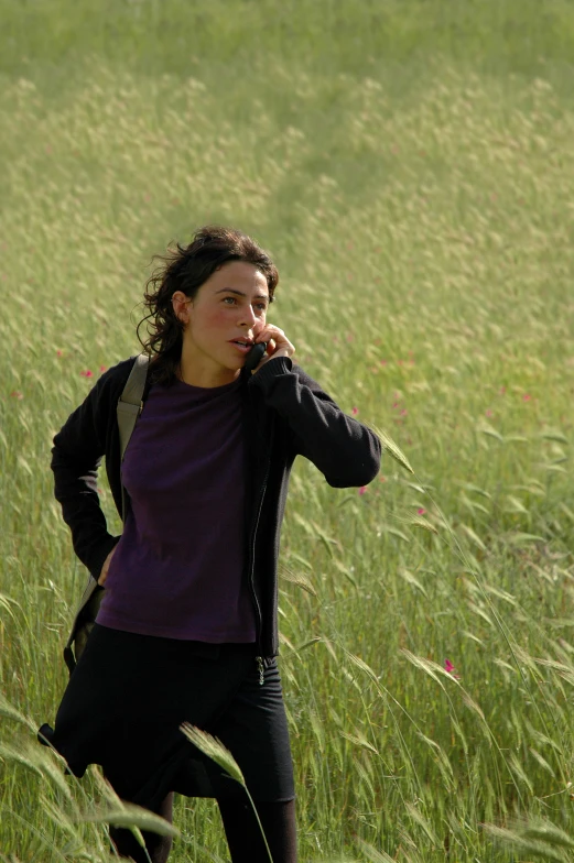 a woman with a backpack on a cellphone is walking through tall grass