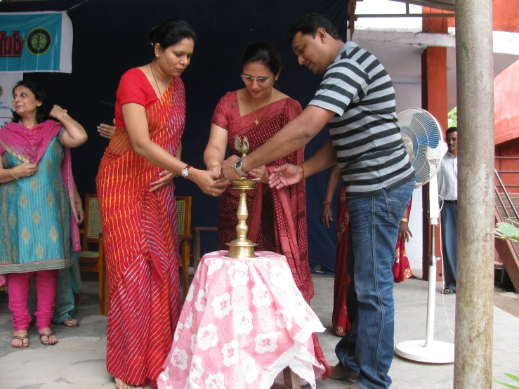 people stand next to each other in the background, a person is holding an ornate lamp while a man holds up another object