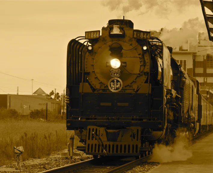 an old - fashioned train rolls by on the tracks through a town