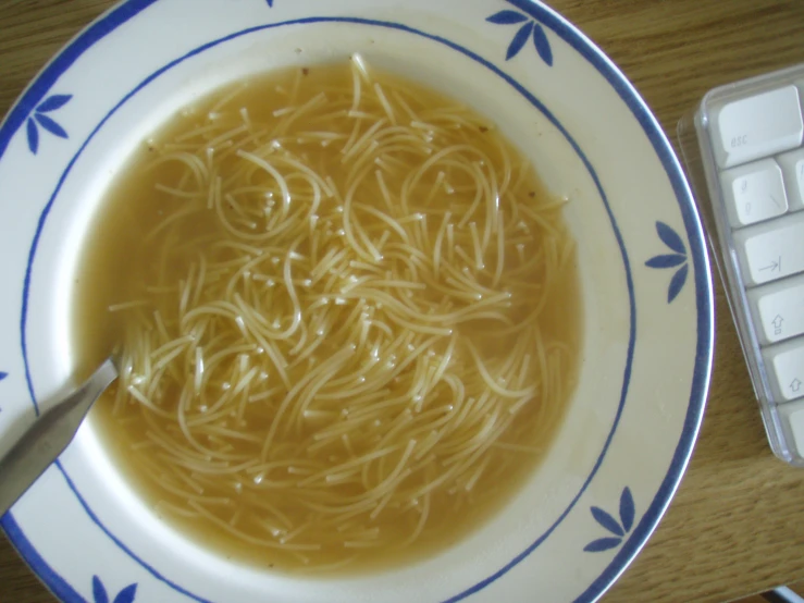 a bowl of noodles in broth on a white and blue plate
