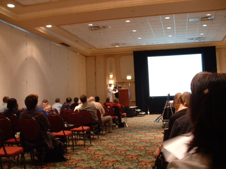 people sit in rows watching a large screen at an event