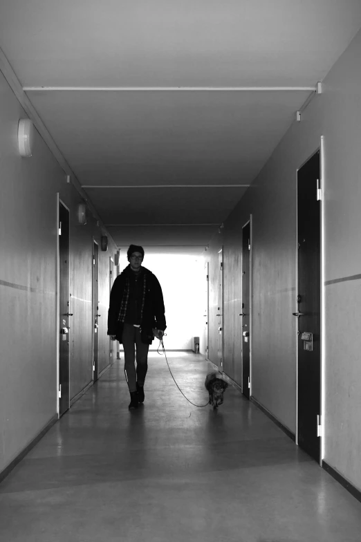 black and white po of a man walking down a corridor with a dog on leash