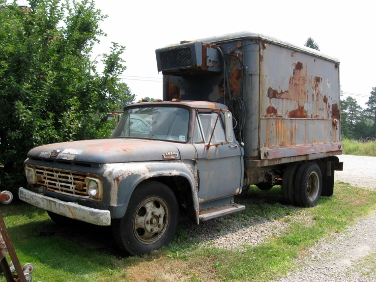 a rusted out truck sitting in a field next to some trees