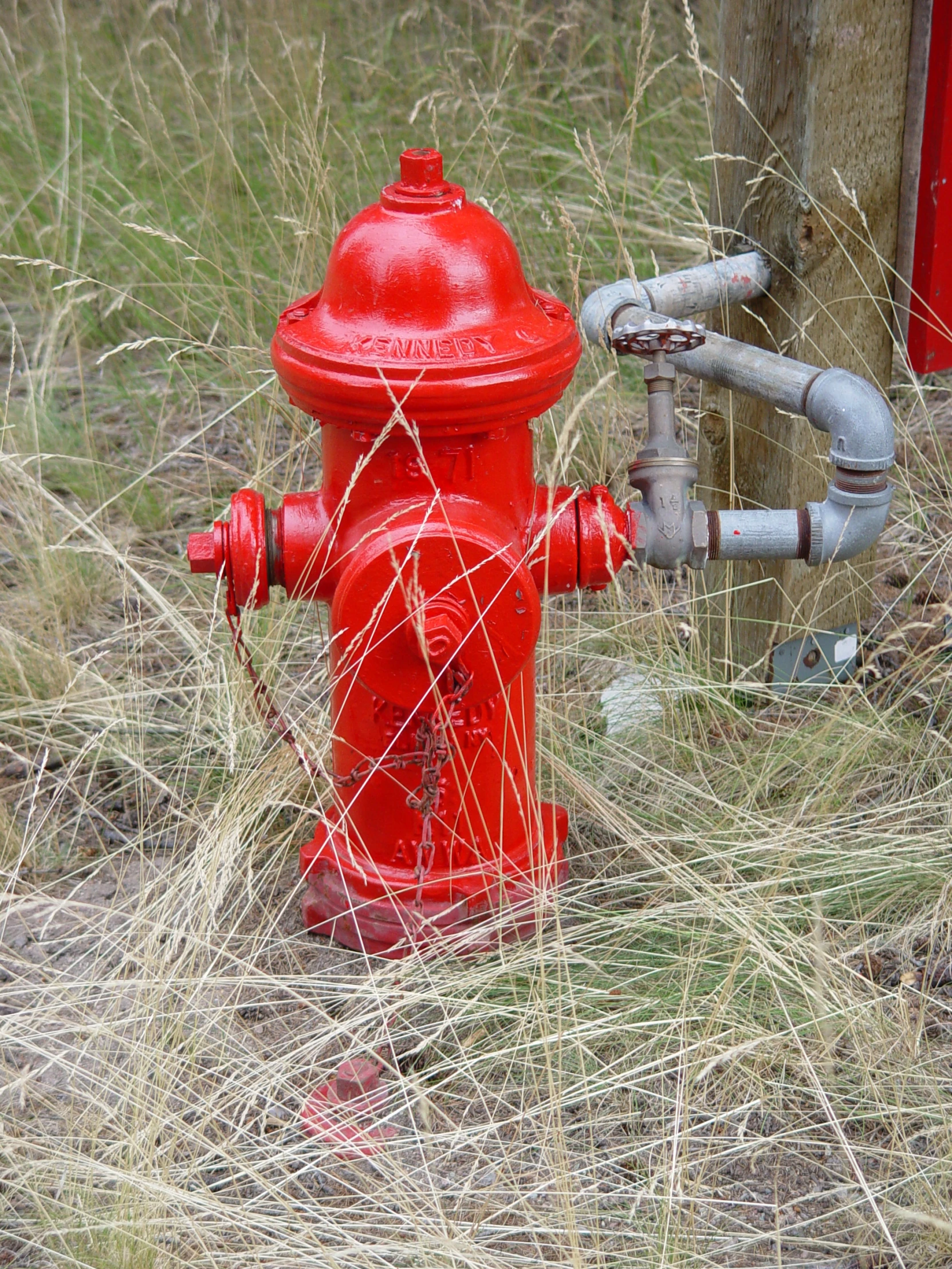 a red fire hydrant next to a post in a field