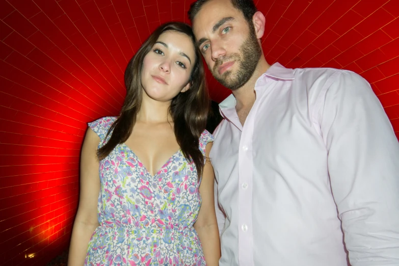 a man and woman are posing in front of a red wall