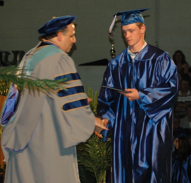 a graduate shakes hands with another person in a regal gown