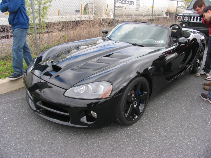 two men standing beside a black sports car