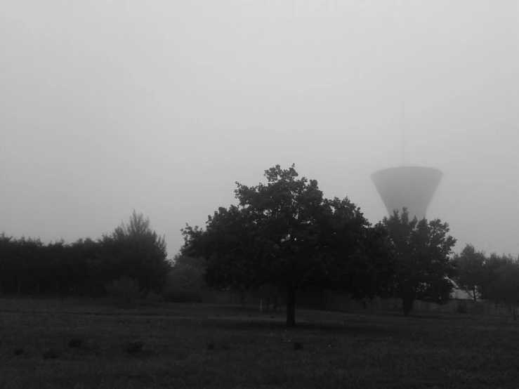 a large water tower in a grassy area under a foggy sky