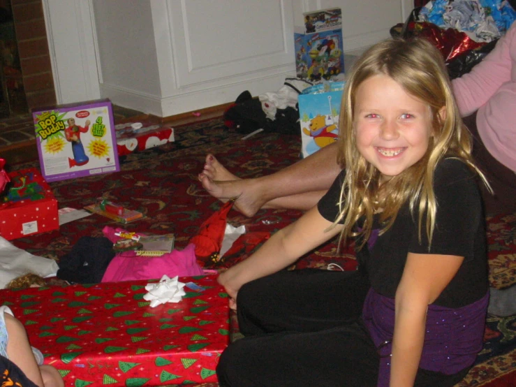 a smiling  in black shirt sitting on the floor with presents