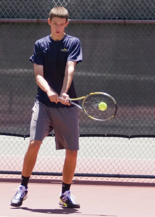 man playing tennis in front of fence with ball