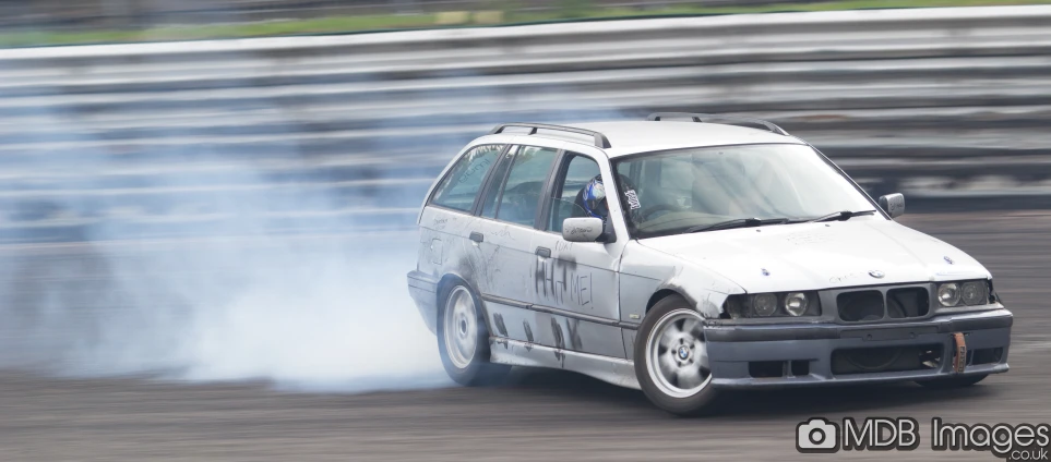 an old bmw car kicking up smoke in a race track