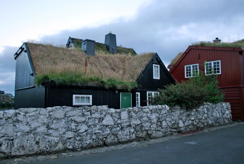 a red house with grass on the roof next to a stone fence